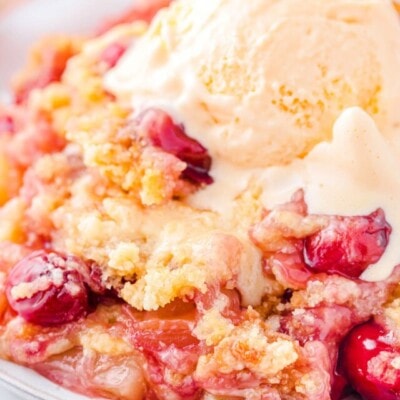 plate filled with cherry pineapple dump cake and topped with a scoop of vanilla ice cream that is just beginning to melt. cherries and pineapple chunks are visible in the cake.