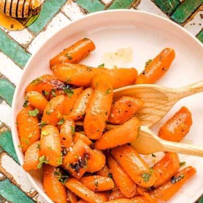 honey glazed carrots on a round white plate garnished with fresh parsley. the plate is on a teal and white chevron tile surface.