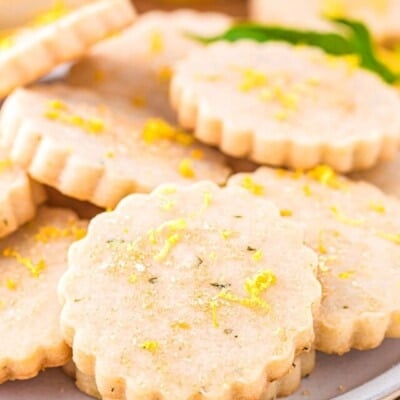 lemon basil shortbread cookies on a white plate topped with lemon zest and coarse sugar.