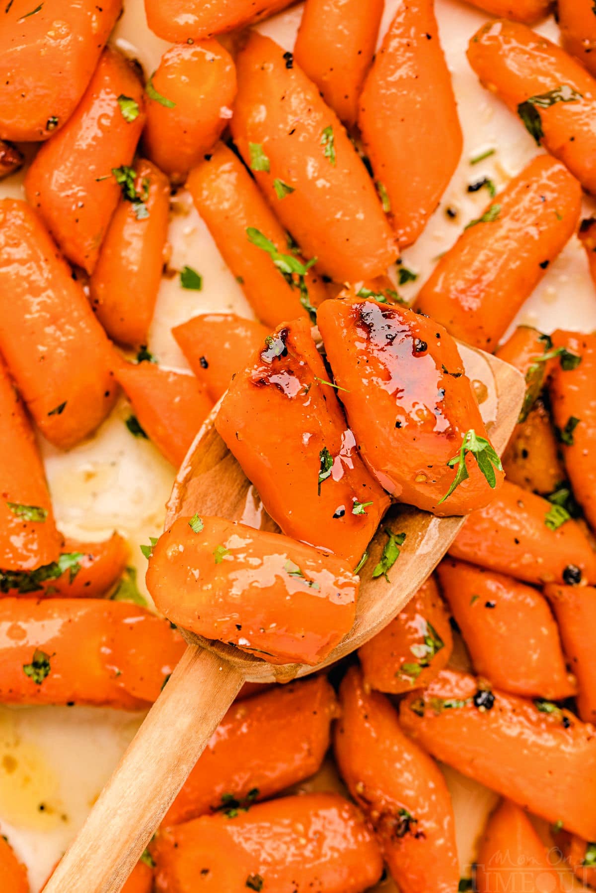 honey glazed carrots on a baking sheet made with honey and garlic. a wood spoon is holding up three carrots.