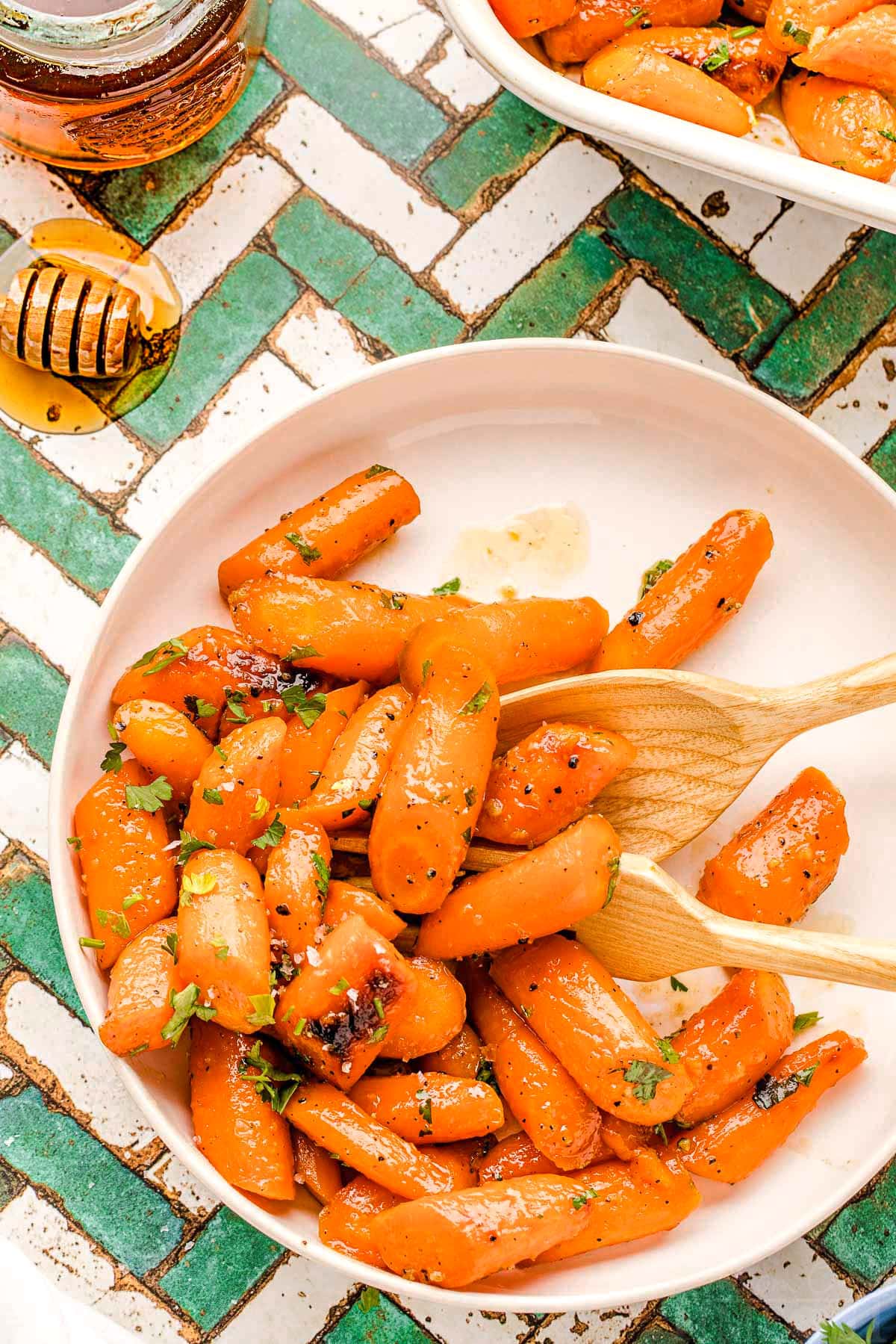 honey glazed carrots on a round white plate garnished with fresh parsley. the plate is on a teal and white chevron tile surface.