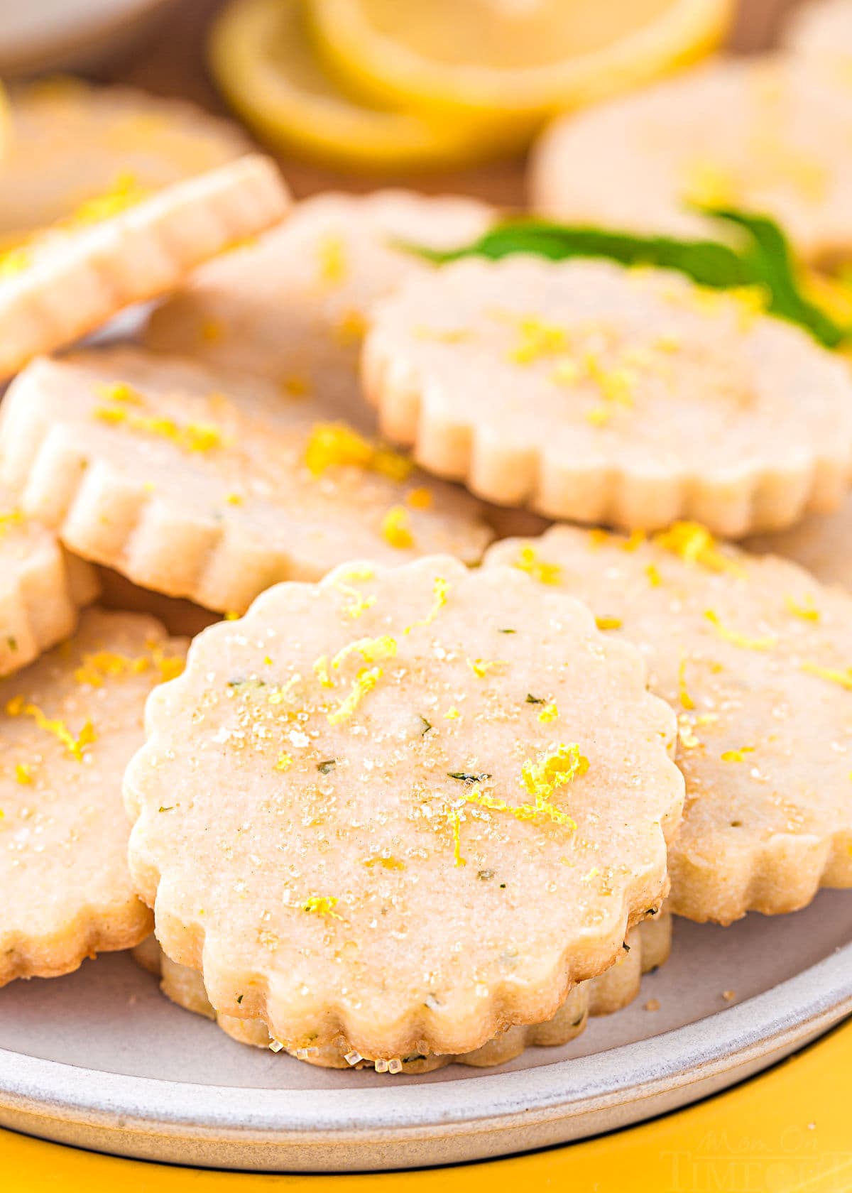 lemon basil shortbread cookies on a white plate topped with lemon zest and coarse sugar. 