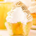 lemon meringue cupcake with bite taken showing the lemon curd in the middle of the cupcake and the pretty white interior of the meringue.