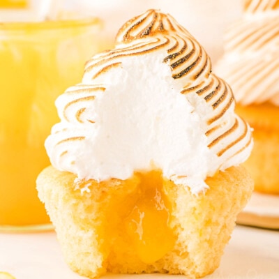 lemon meringue cupcake with bite taken showing the lemon curd in the middle of the cupcake and the pretty white interior of the meringue.