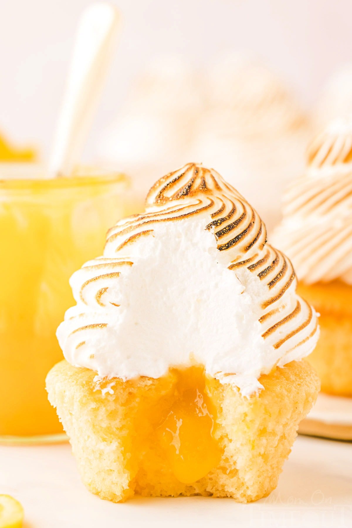 lemon meringue cupcake with bite taken showing the lemon curd in the middle of the cupcake and the pretty white interior of the meringue.