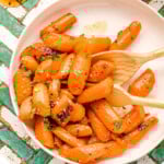 honey glazed carrots on a round white plate garnished with fresh parsley. the plate is on a teal and white chevron tile surface.