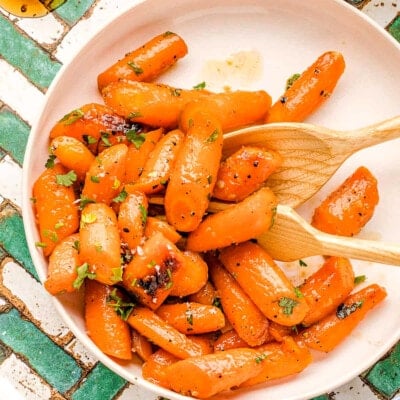 honey glazed carrots on a round white plate garnished with fresh parsley. the plate is on a teal and white chevron tile surface.