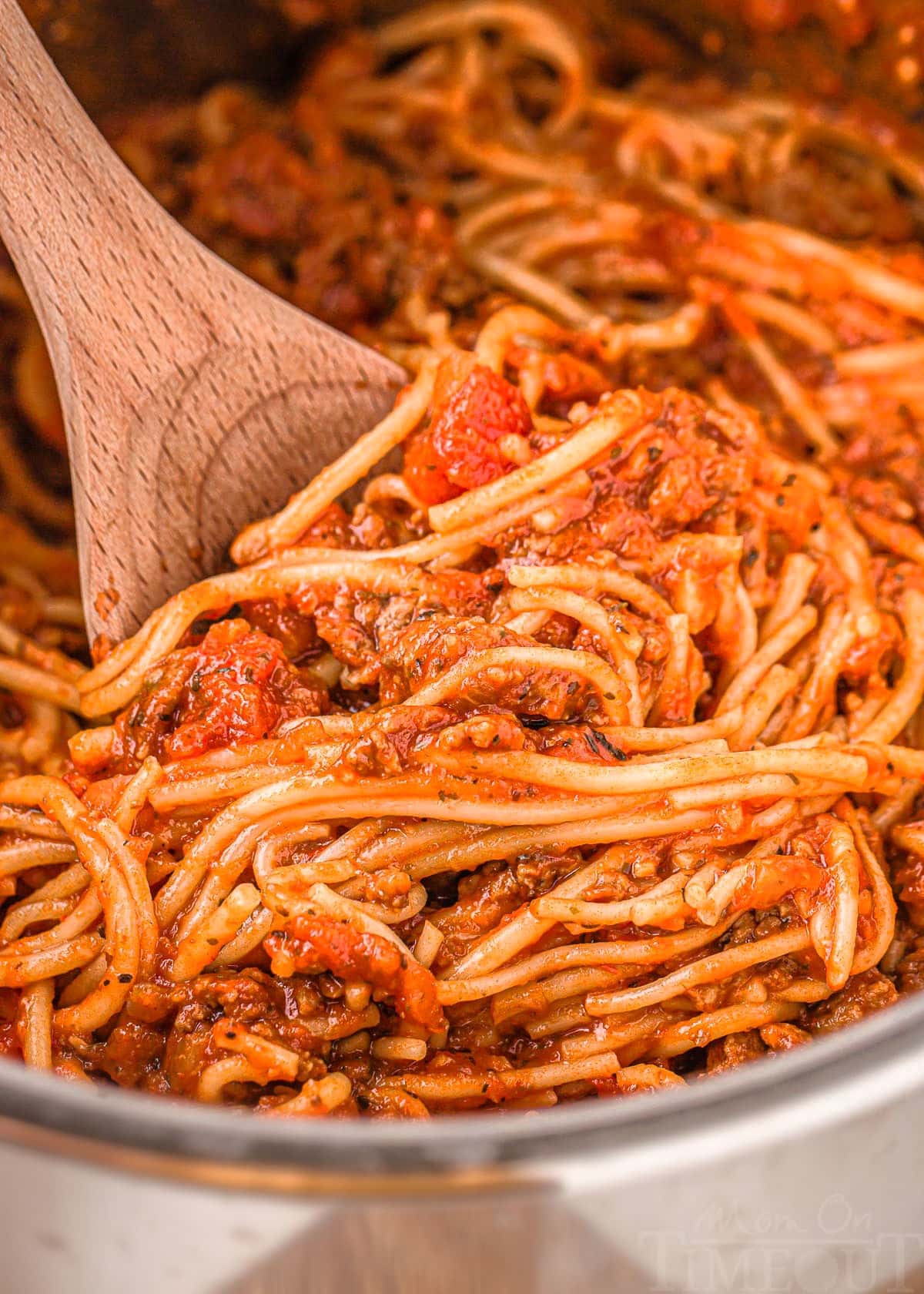 close up look at instant pot with spaghetti in it ready to be served with a wooden spoon.