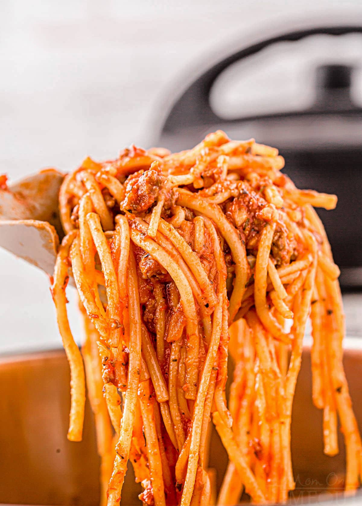 scoop of instant pot spaghetti with the sauce mixed in held up over the instant pot.