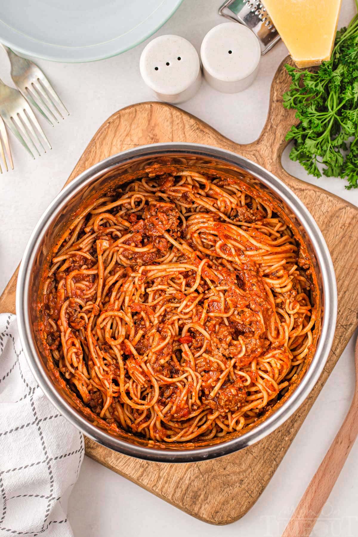 spaghetti in instant pot ready to be served sitting on a wood cutting board with parsley and parmesan next to the board.