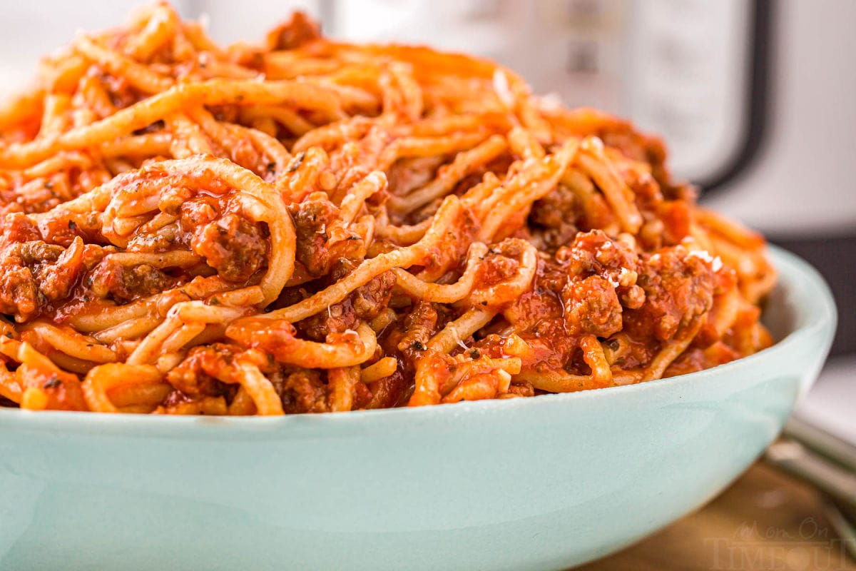 large aqua serving bowl generously filled with spaghetti and meat sauce.