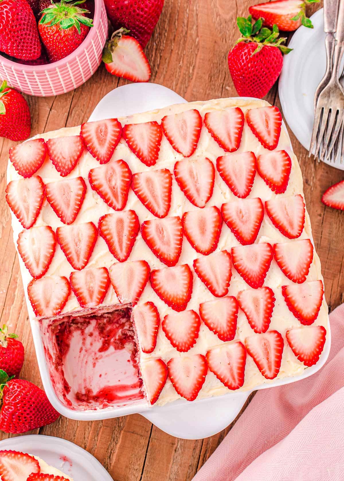 top down look at assembled strawberry tiramisu in white baking dish sitting on wood board with one serving removed.