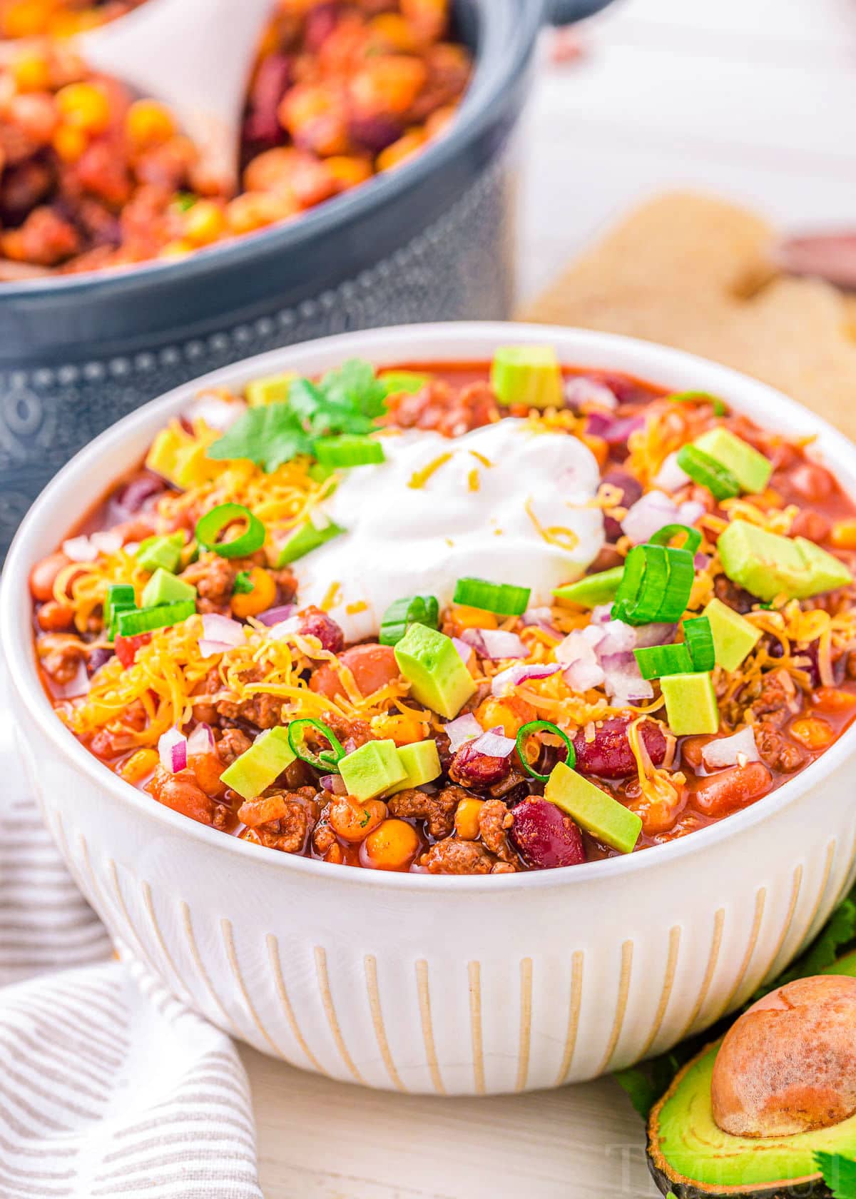 taco soup in white bowl with toppings including cheese, sour cream and red onions. blue dutch oven can be seen in the background.