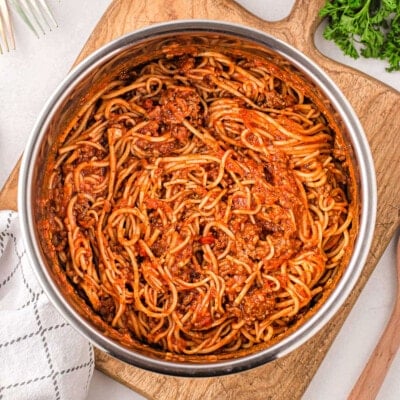 spaghetti in instant pot ready to be served sitting on a wood cutting board with parsley and parmesan next to the board.