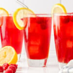 three tall glasses filled with raspberry iced tea and topped with a lemon slice.