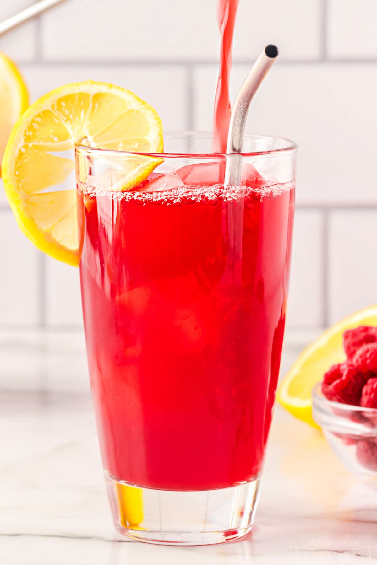 raspberry tea being poured into a tall glass.