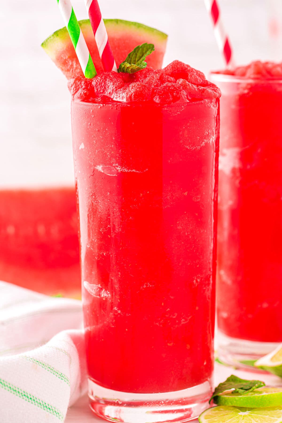 two tall glasses filled with bright red watermelon slushie and topped with a watermelon wedge.