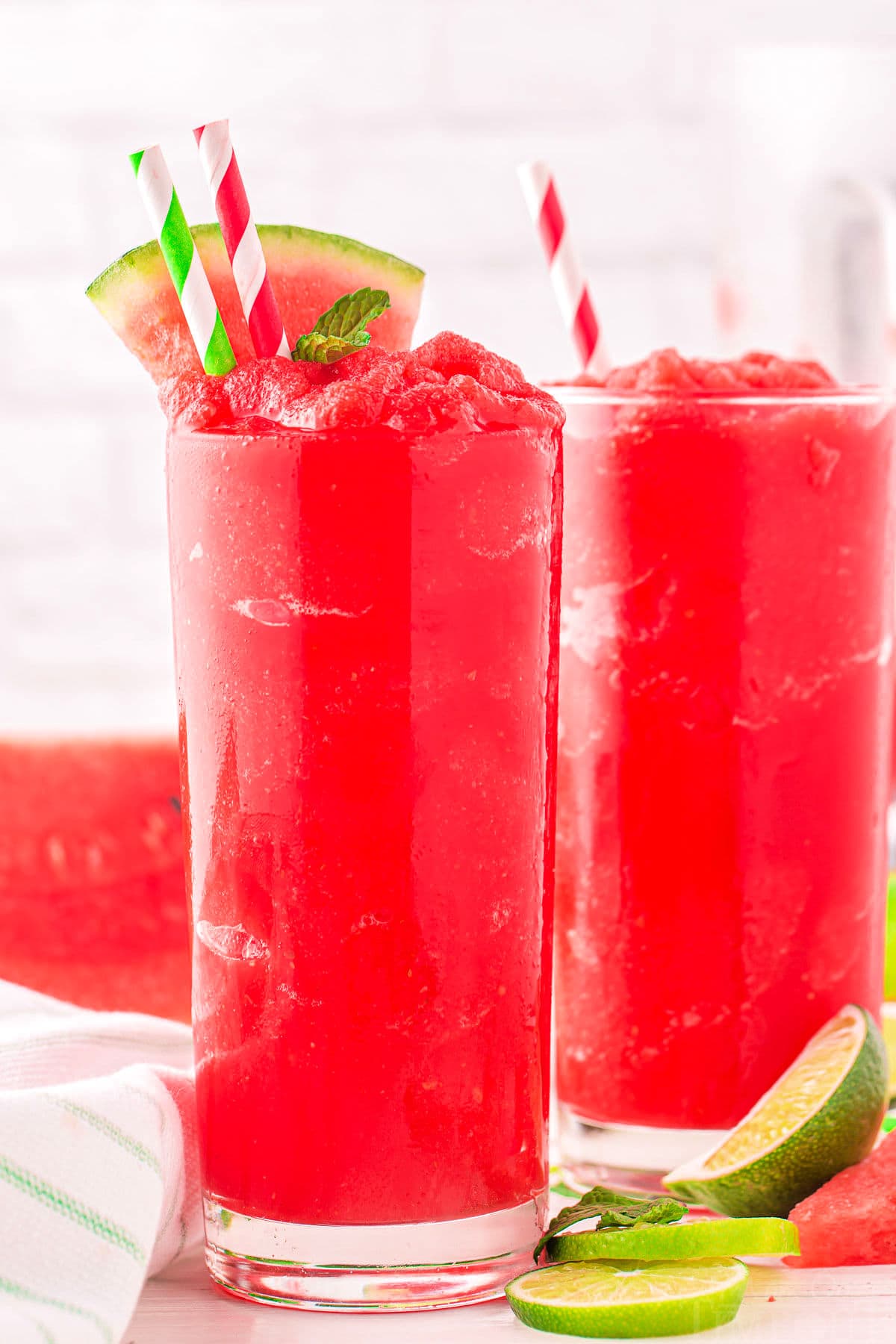 two tall glasses filled with bright red watermelon slushie and topped with a watermelon wedge. 