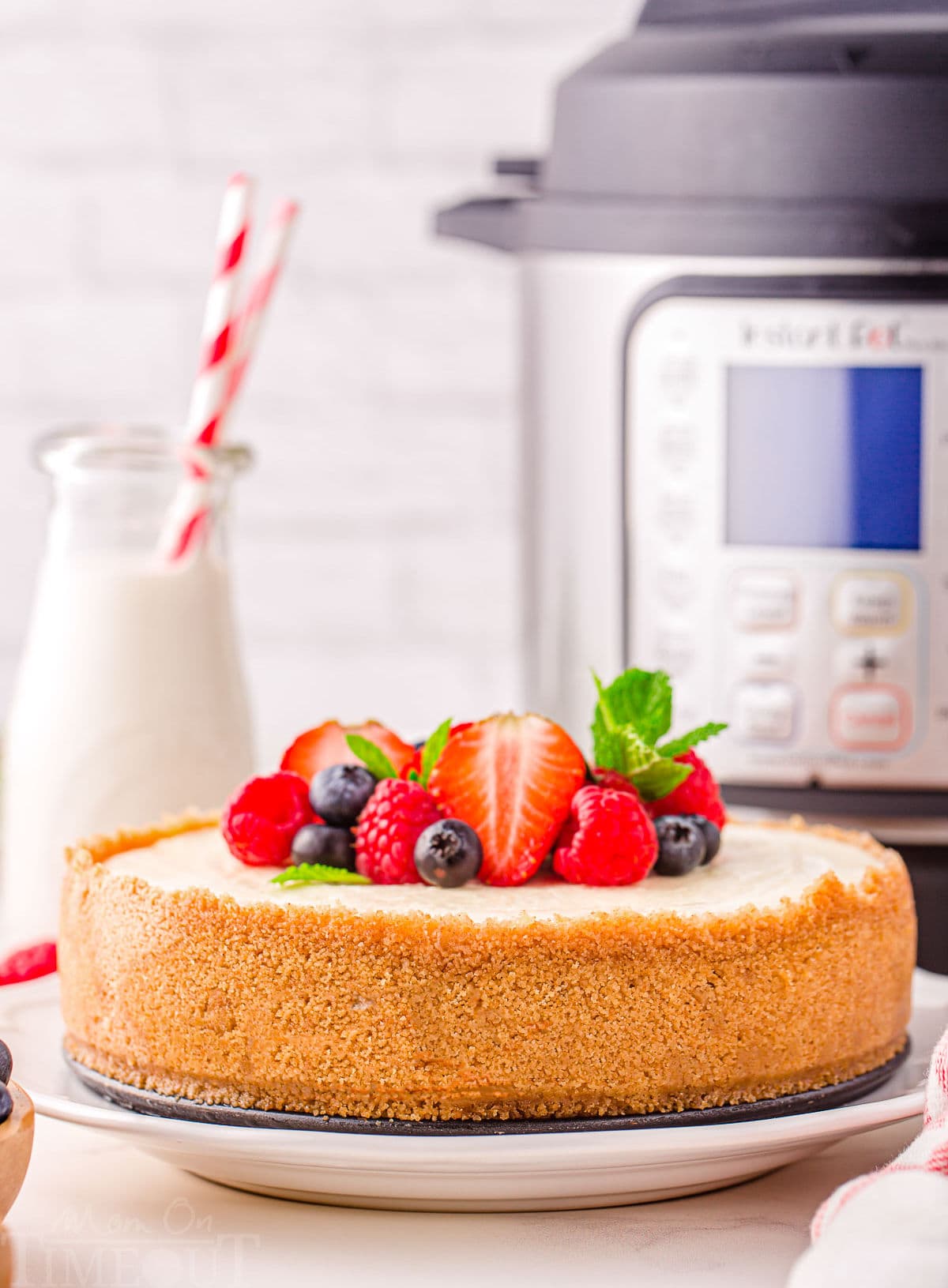 whole cheesecake sitting in front of instant pot with berries on top.