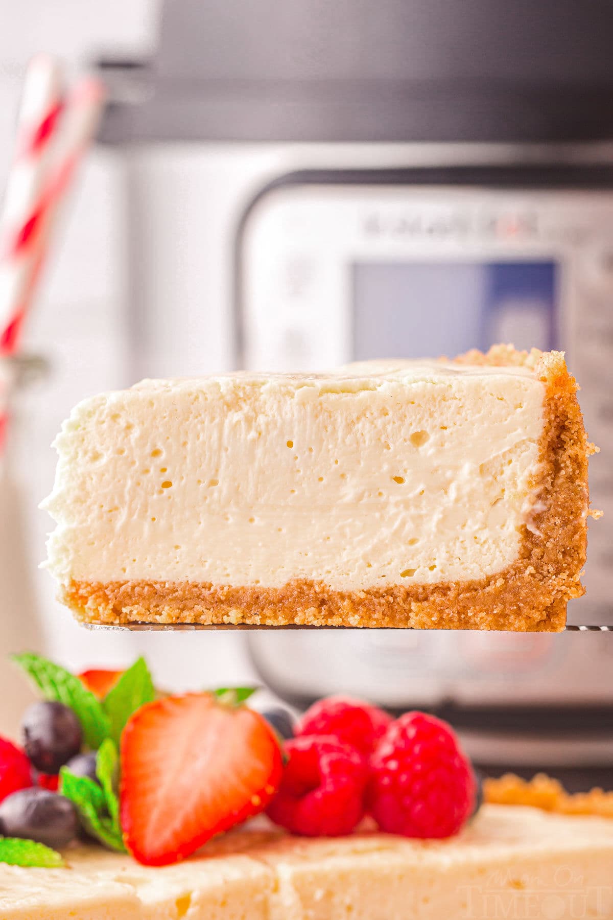 one slice of instant pot cheesecake being held above the rest of the cheesecake in front of an instant pot.