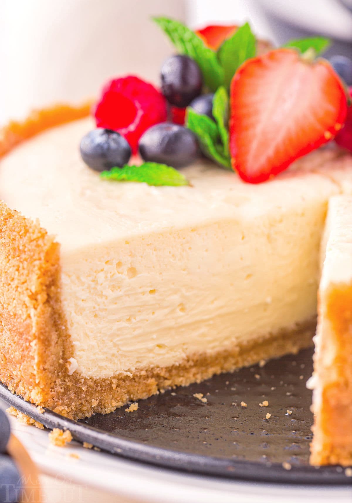 close up look at interior of cheesecake with one slice removed. fresh berries and mint can be seen on top of the cheesecake.