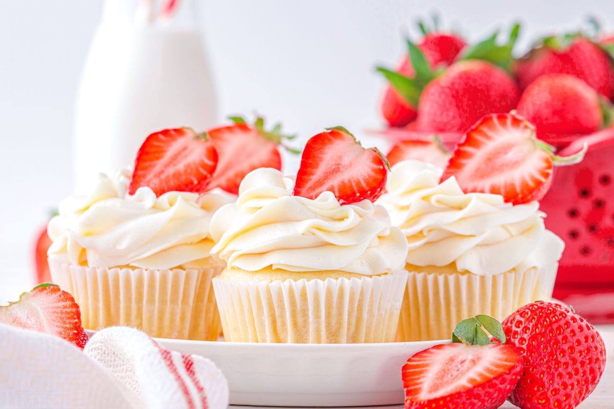 five vanilla cupcakes topped with vanilla buttercream and filled with strawberry jam on white plate.