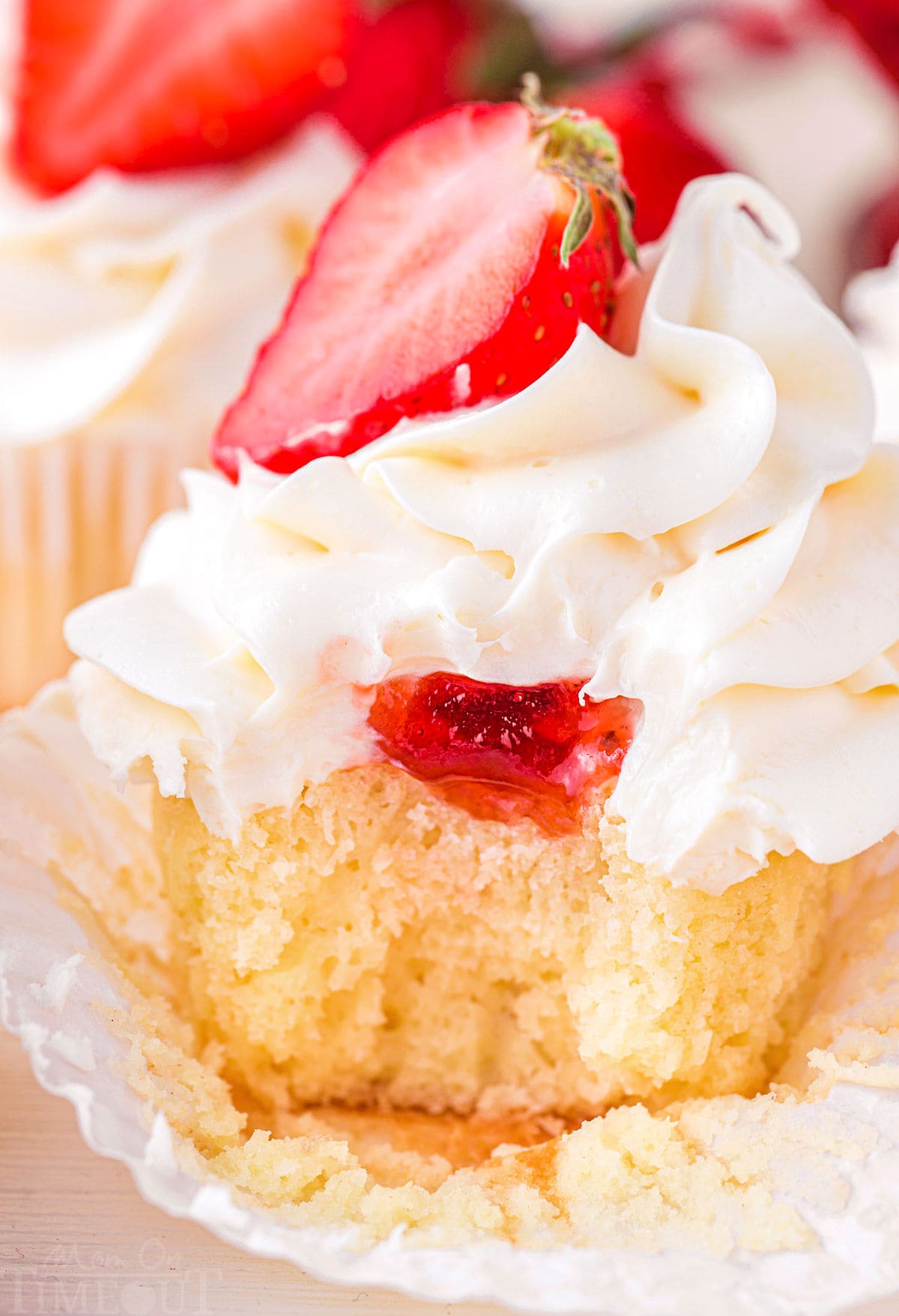 close up look at strawberry filling in a strawberry shortcake cupcake topped with vanilla buttercream frosting.