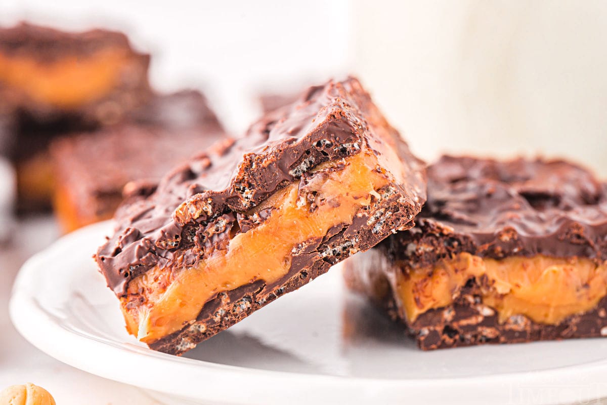 two chocolate caramel bars on a white plate with one bar leaning up on the other. more bars can be seen in the background.