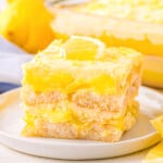 layered lemon tiramisu dessert cut into a square on a white dessert plate with the rest of the dessert in the background.