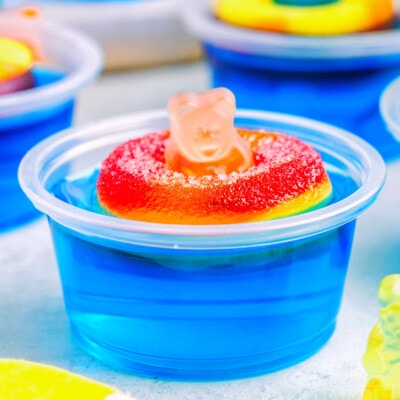 blue pool party jello shot with gummi bear sitting on white surface. more jello shots can be seen in the background.