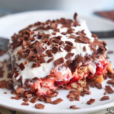 layered dessert made with cherry pie filling and whipped cream. four layers on a white plate topped with chocolate shavings.