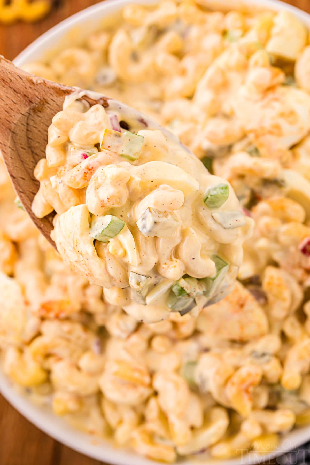 wood spoon with a large scoop of macaroni salad being held above the serving bowl.