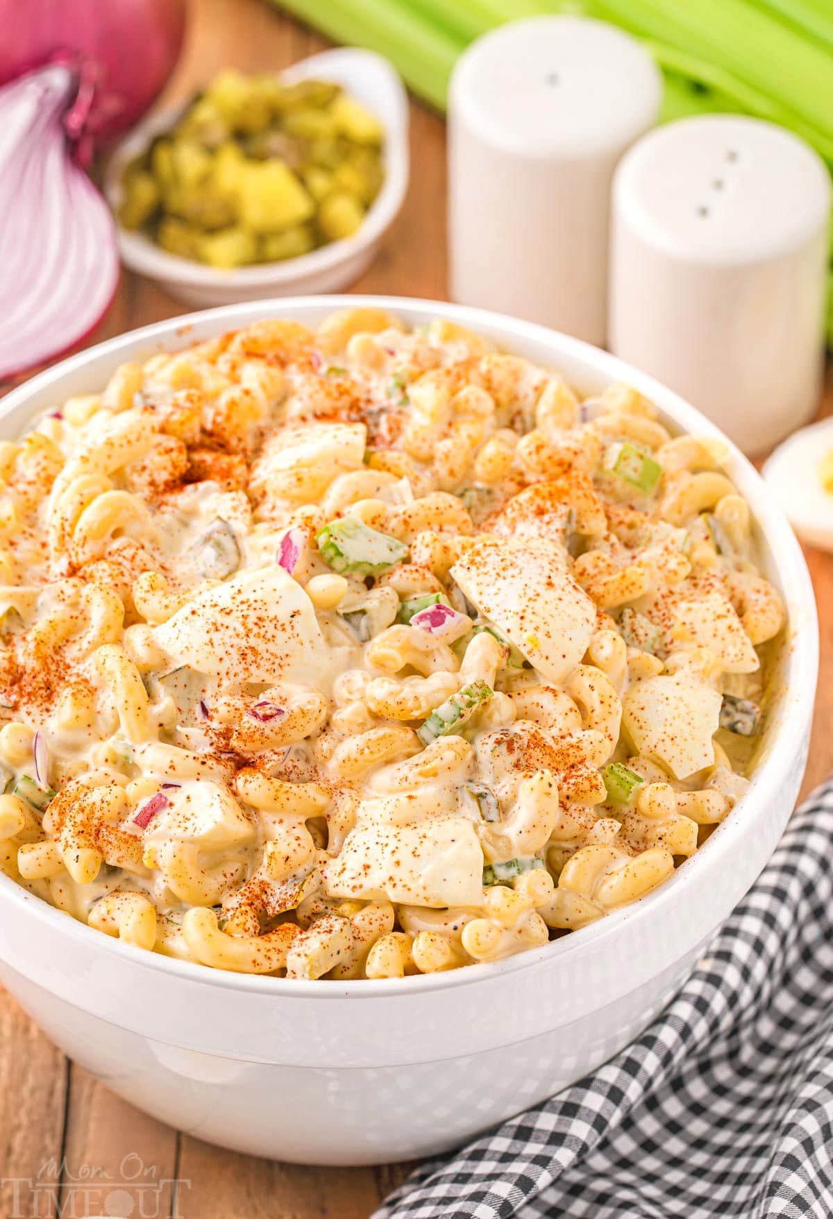 deviled egg macaroni salad in a white bowl topped with paprika. red onion, pickles and celery can be seen in the background.