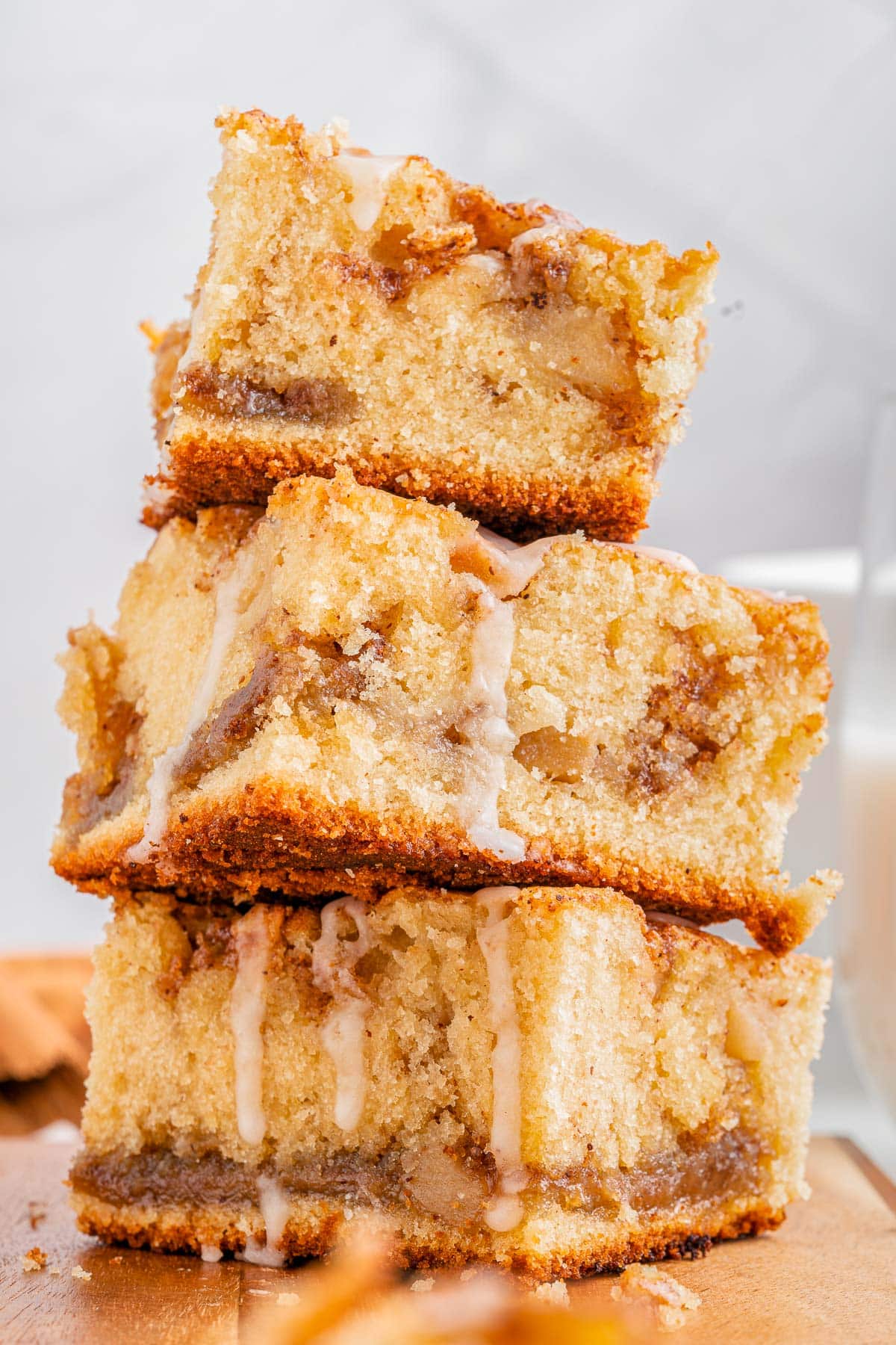 three pieces of apple coffee cake stacked on a wood cutting board. glaze is drizzled down on top of the coffee cake pieces.