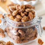 candied almonds in a glass jar filled to overflowing. a small white bowl of candied almonds can be seen in the background.