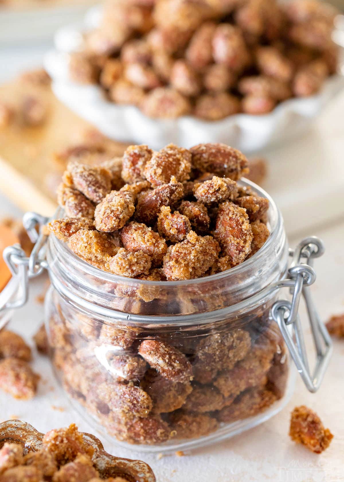 candied almonds in a glass jar filled to overflowing. a small white bowl of candied almonds can be seen in the background.