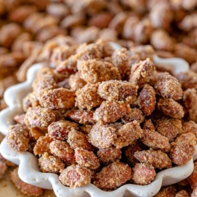 homemade candied almonds recipe in a small white bowl surround with more almonds on a sheet pan.