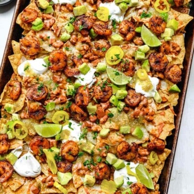 top down look at shrimp nachos prepared on a sheet pan topped with sour cream, avocados and salsa.