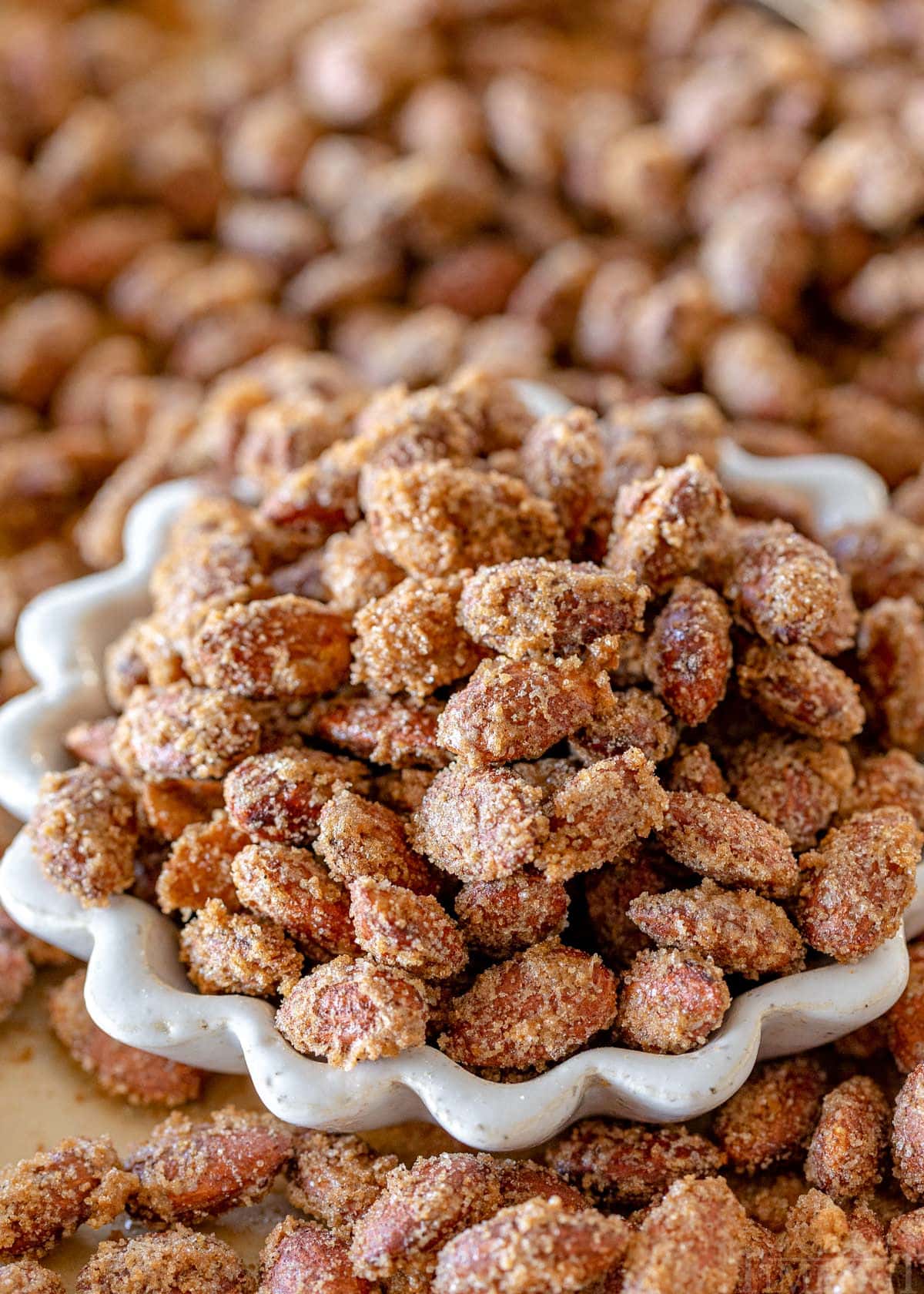 homemade candied almonds recipe in a small white bowl surround with more almonds on a sheet pan.