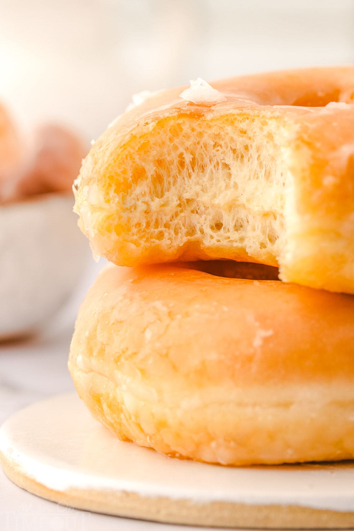 two yeast donuts with glaze stacked on each on a small white plate with bite taken from top donut.