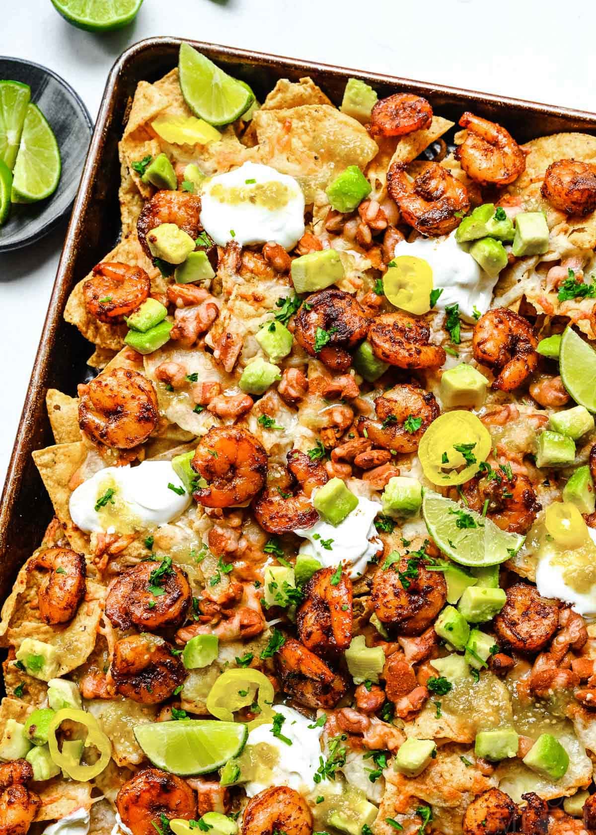 top down look at shrimp nachos prepared on a sheet pan topped with sour cream, avocados and salsa.