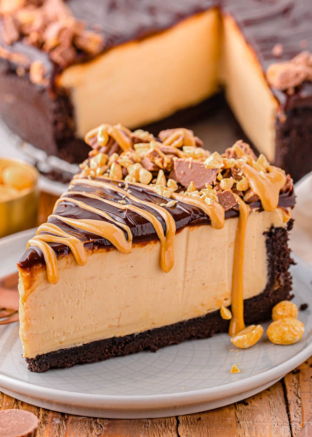 single slice of peanut butter cheesecake sitting on small round white plate. cheesecake is topped with peanut butter topping and reese's peanut butter cups chopped up.