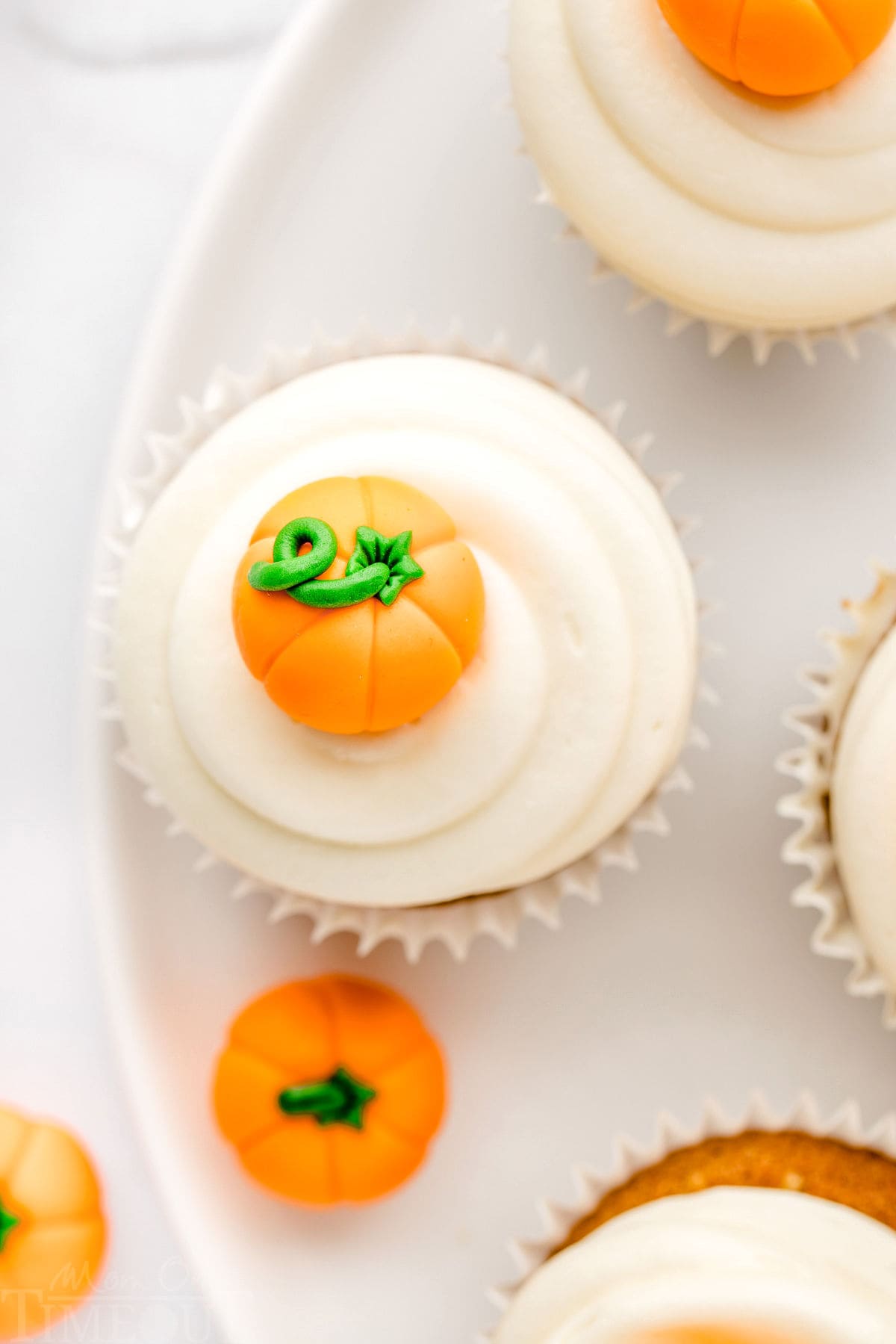 top down look at pumpkin cupcakes on a white plate topped with cream cheese frosting and candy pumpkins.