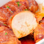 baking dish with bacon wrapped chicken. one chicken breast is cut in half. the chicken is topped with parsley.