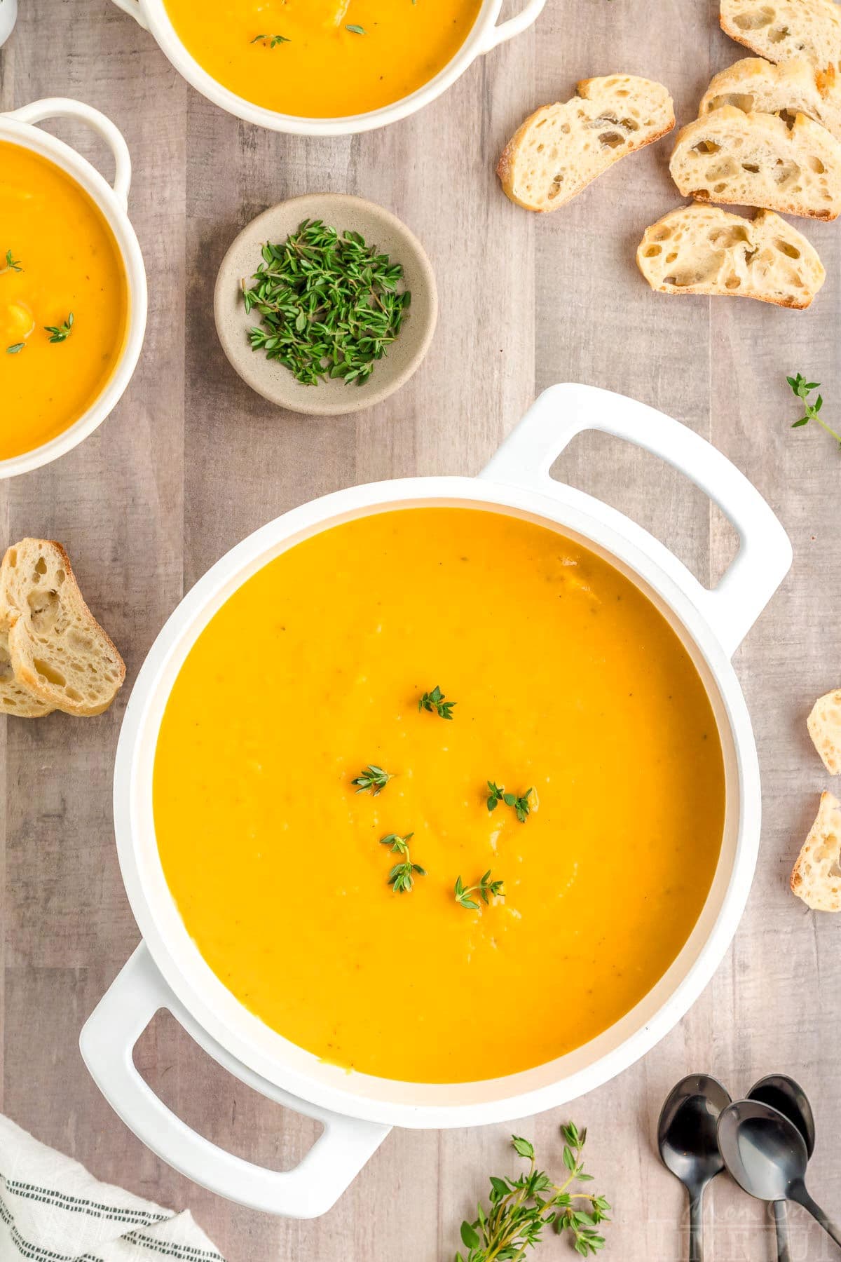 top down view of butternut squash soup in large white bowl with two smaller white bowls to the side. 