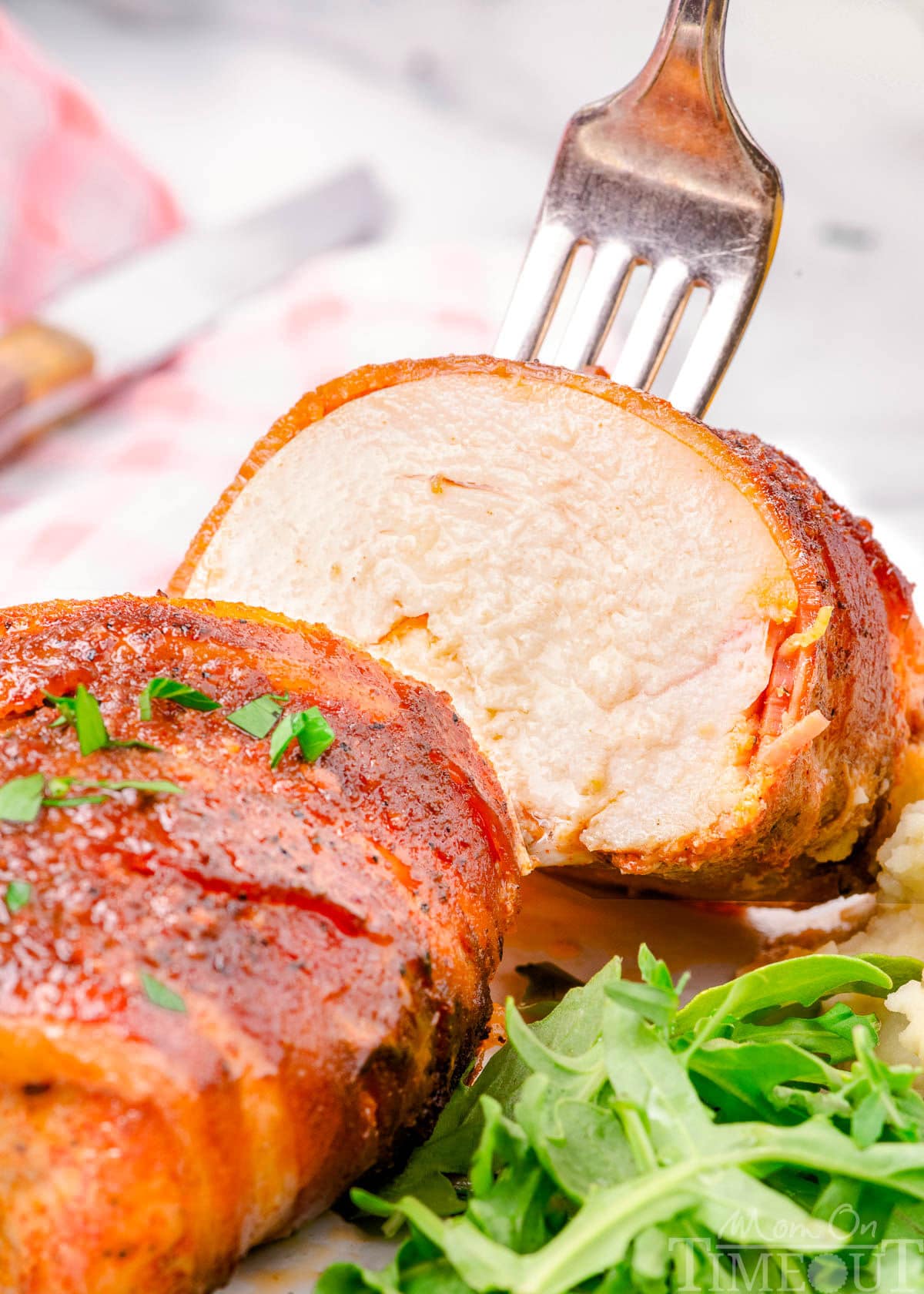 bacon wrapped chicken breast cut in half with fork lifting one half off the plate.