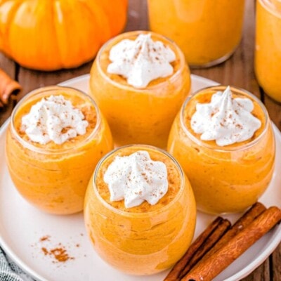 top down angled view of four glasses filled with pumpkin mousse topped with whipped cream.