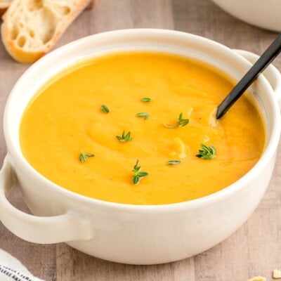 white round bowl filled with butternut squash soup topped with fresh thyme. a black spoon is in the bowl.