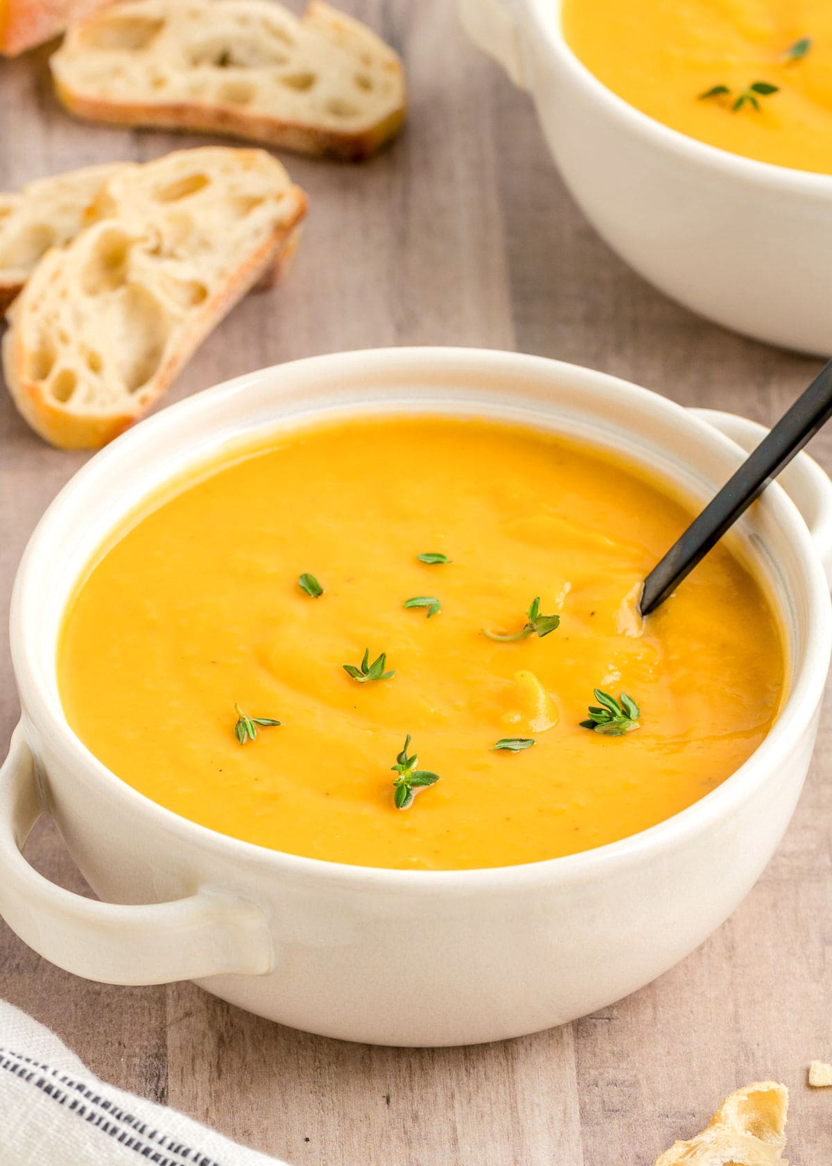 white round bowl filled with butternut squash soup topped with fresh thyme. a black spoon is in the bowl.