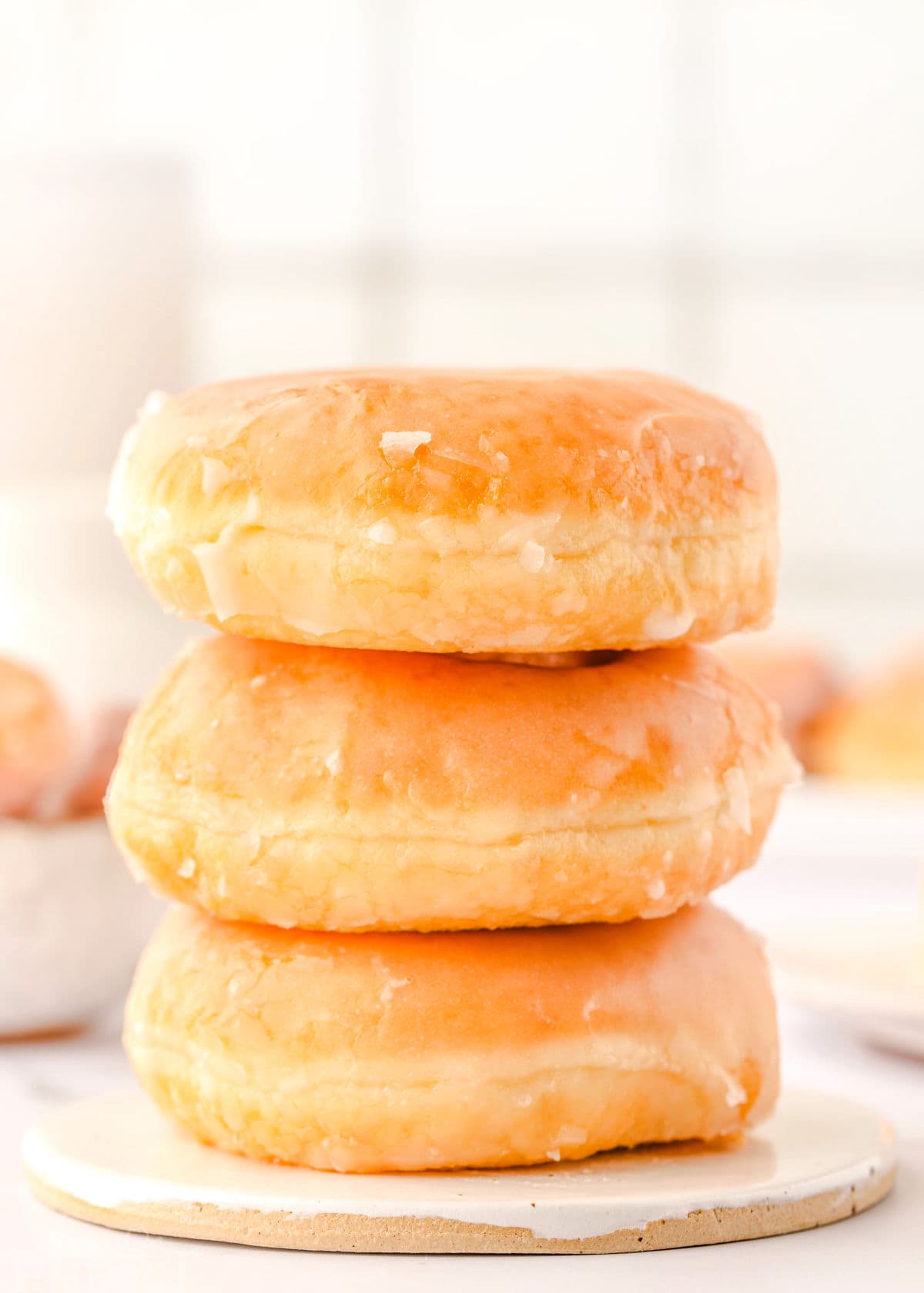 three whole glazed donuts stacked on small white round plate.